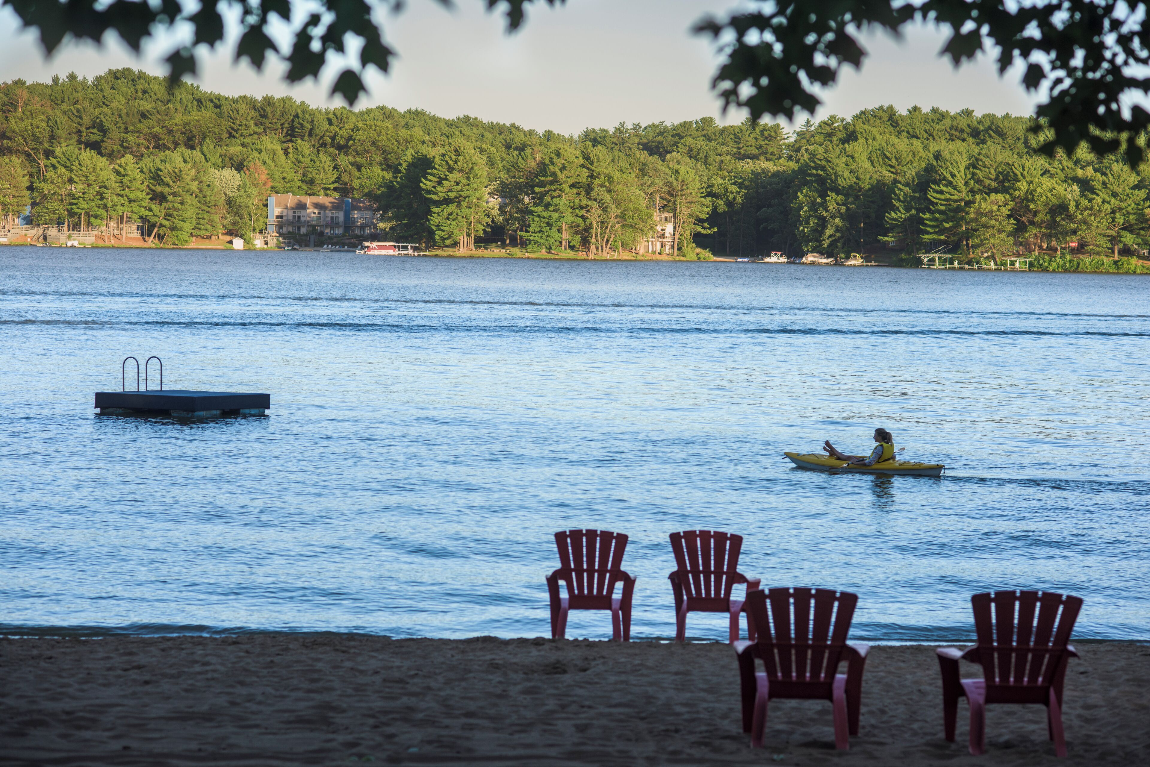 A lakeside view with a dock, chairs, and a kayak.