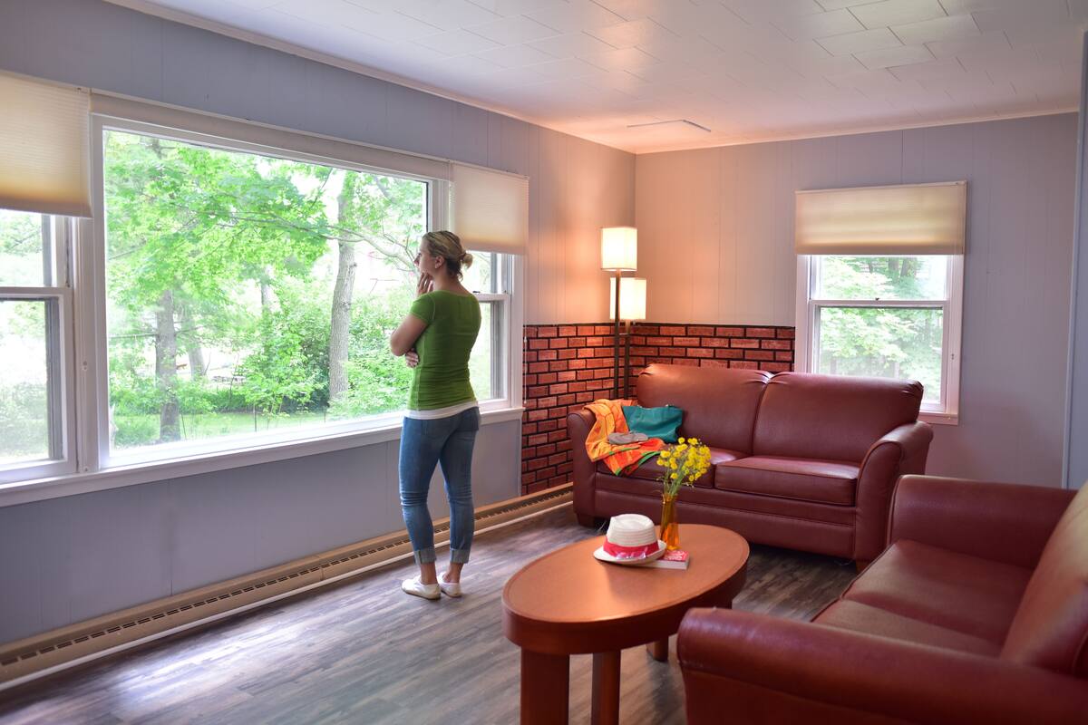 A room with a large window, a brick fireplace, a red leather sofa, and a small table with a vase of flowers.