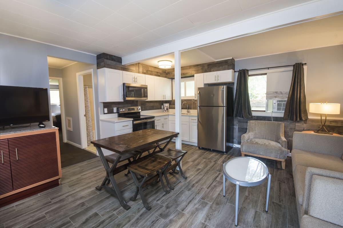 A compact kitchen with modern appliances, a dining area with a wooden table and bench, and a small round table.