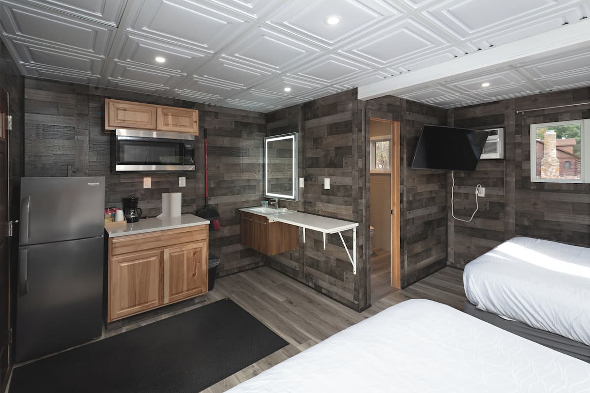 A compact hotel room with a kitchenette, a bed, a TV, and a window with a view.