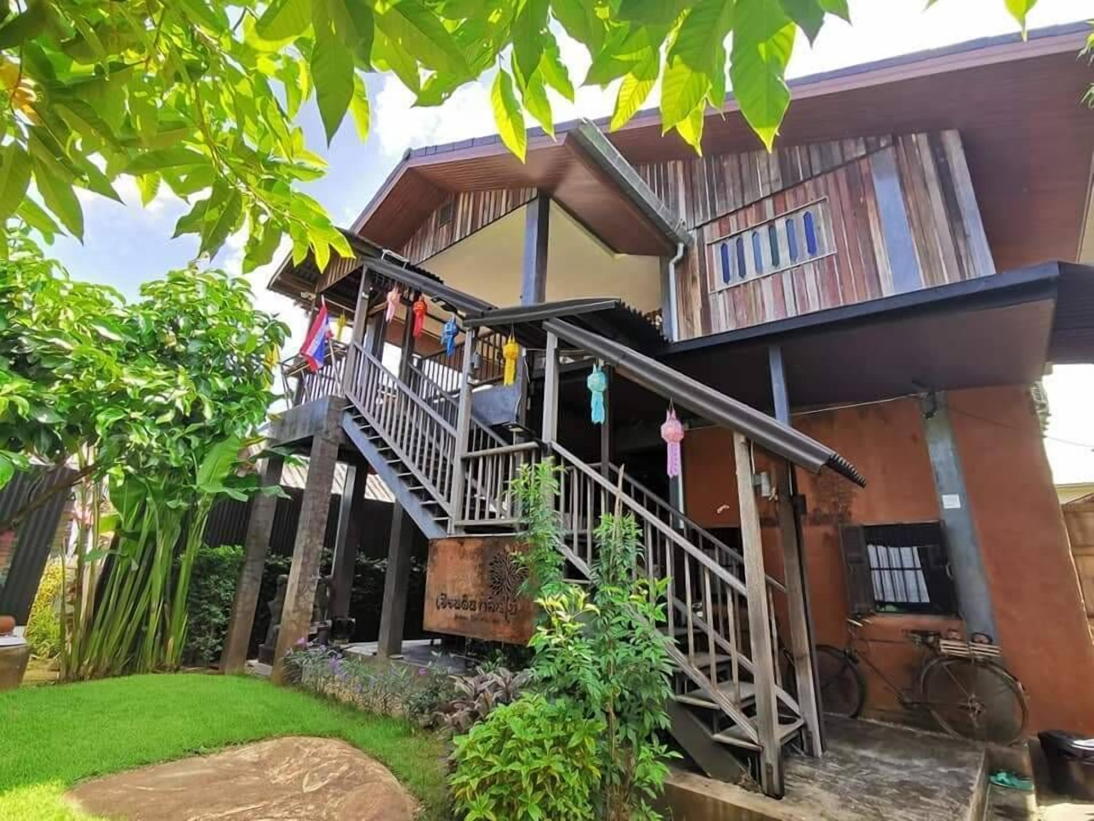 A two-story building with a staircase leading to the upper floor, surrounded by greenery and a small garden.