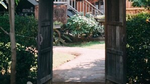 A wooden archway with a sign, leading to a building with a staircase and a view of a garden. - Hueandin Klinmai Boutique Hotel (Chiang Mai)
