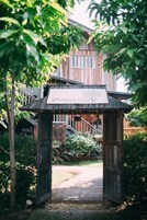 A wooden archway with a sign, leading to a building with a staircase and a view of a garden.
