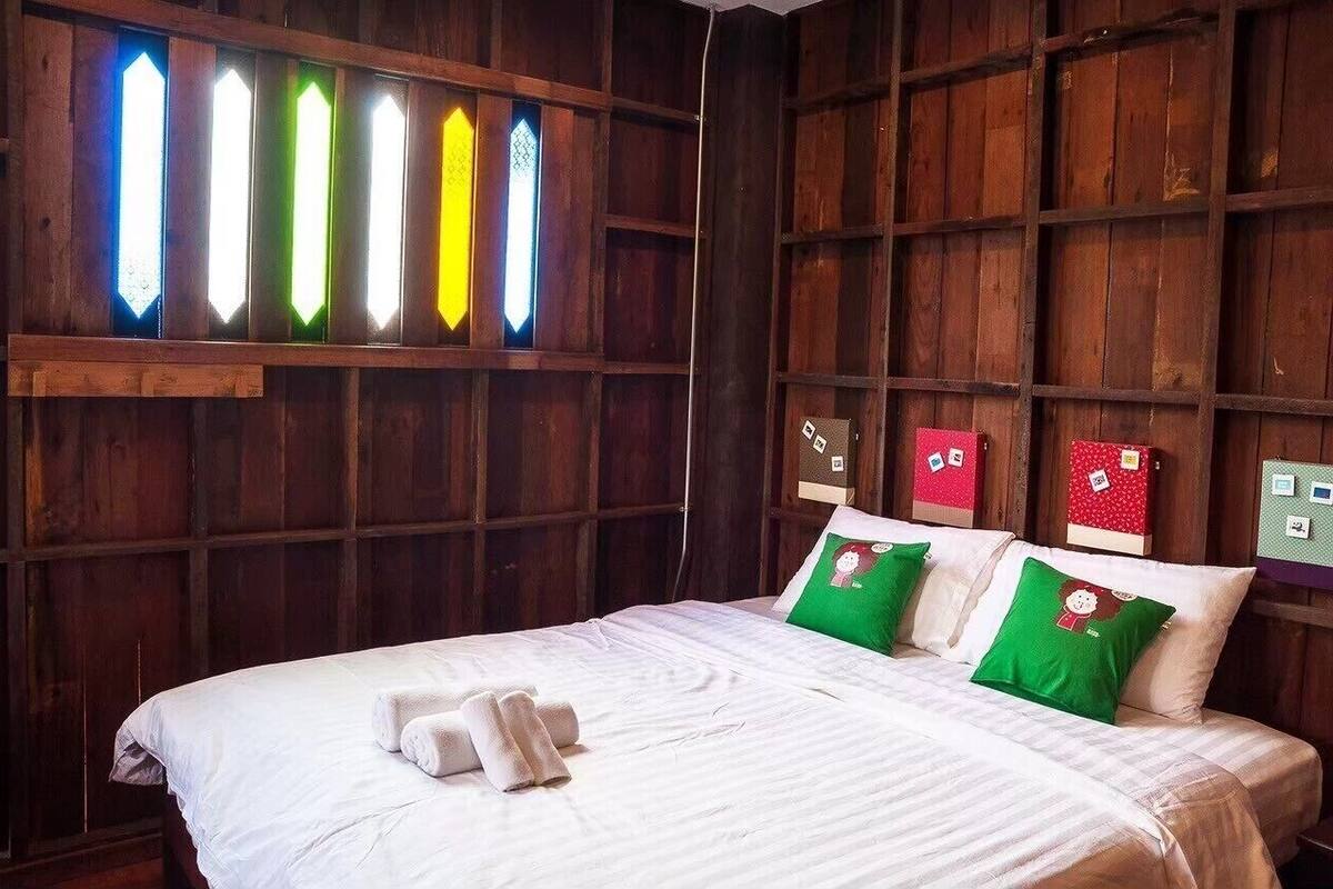 A hotel room with a wooden wall, a bed with white bedding, green and red pillows, and a stained glass window.