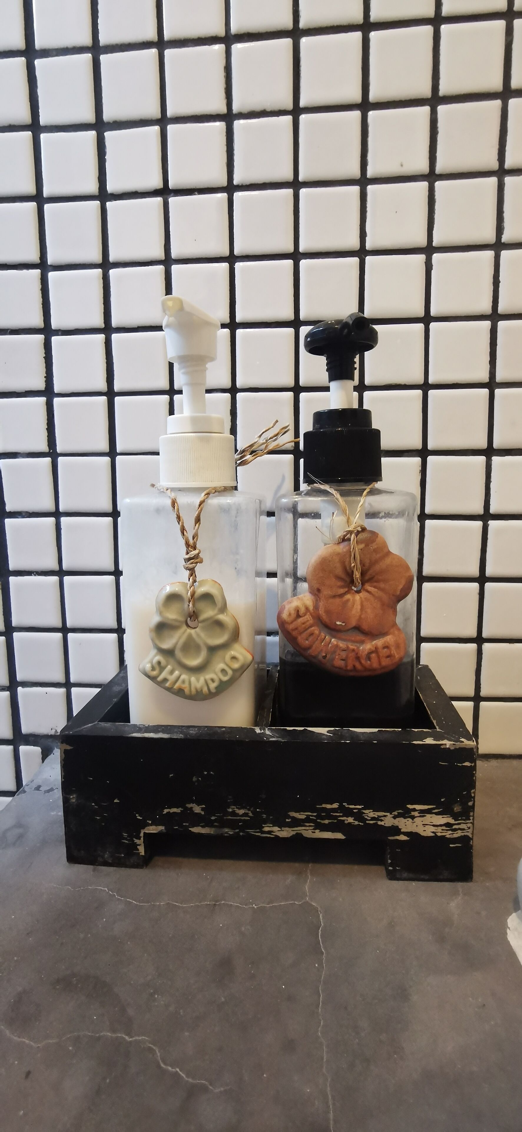 Two glass bottles with pump dispensers, each labeled with a different brand of shampoo, placed on a black crate.
