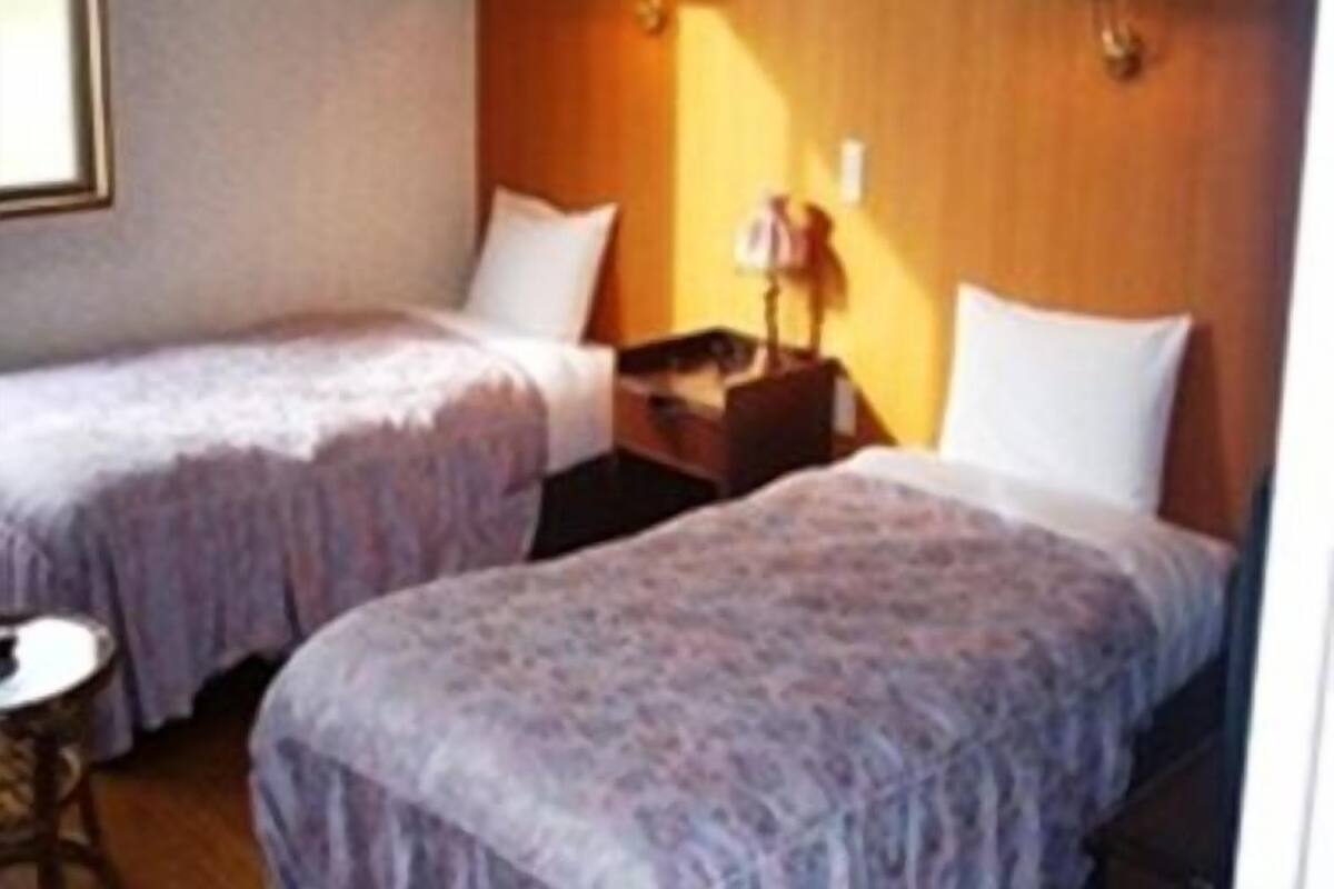 A hotel room with two single beds, a small round table, and a nightstand with a lamp.