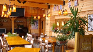 A cozy restaurant with wooden tables and chairs, hanging lights, and various plants. - Charade Inn Shiga (Yamanouchi)
