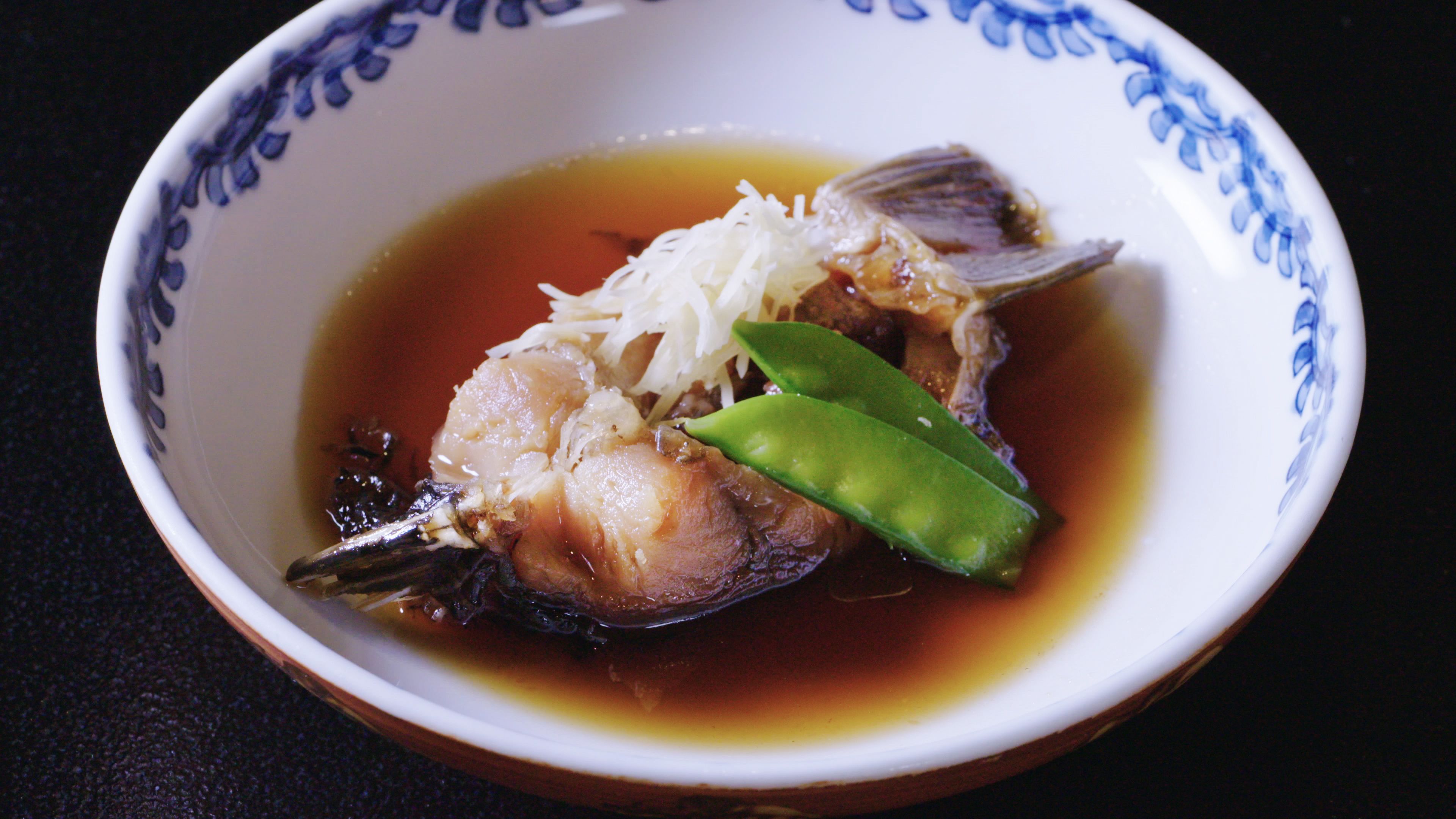 A bowl of fish with shredded vegetables and a green vegetable on a dark surface.