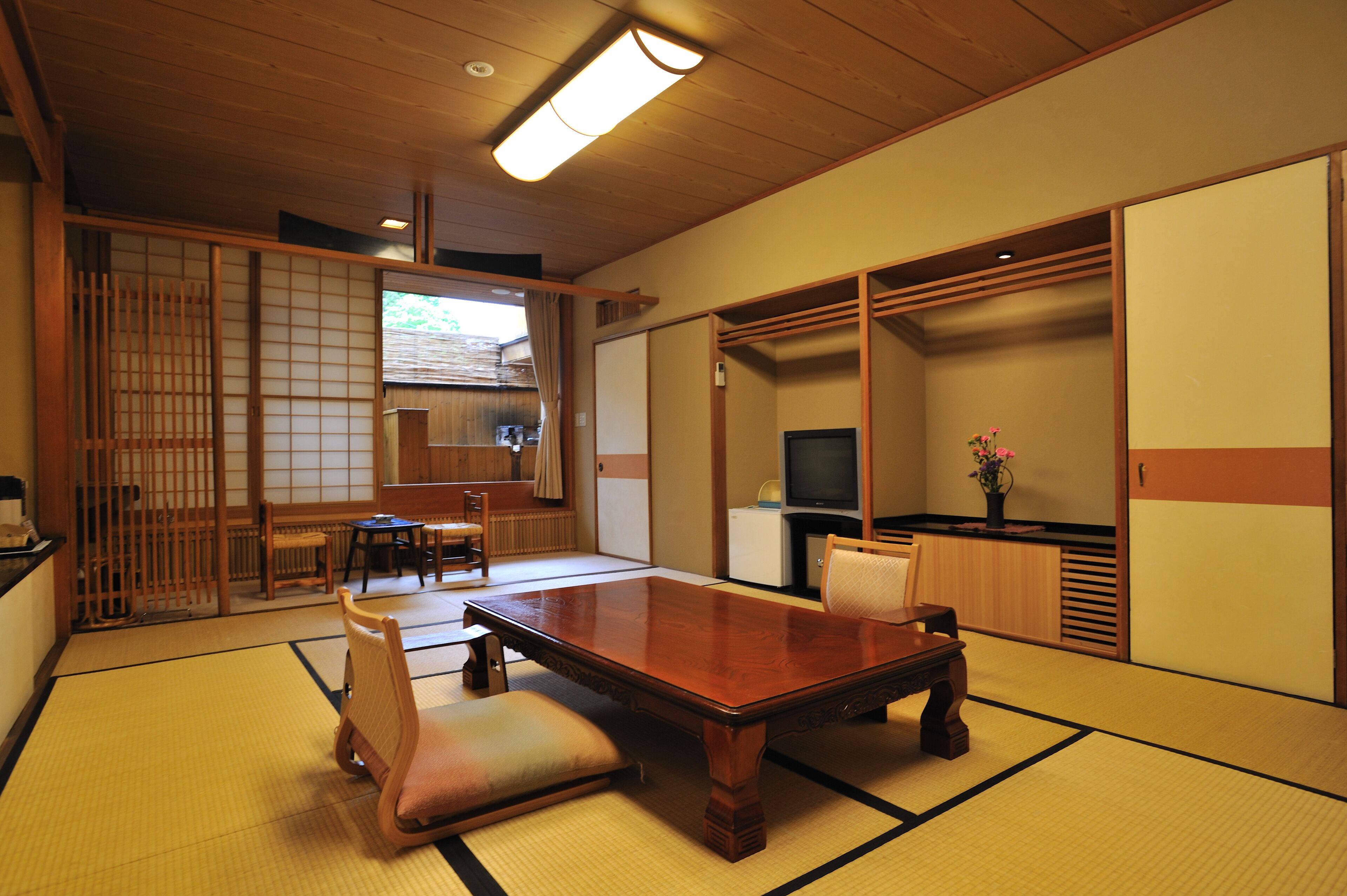 Une pièce de style japonais traditionnel, avec un sol recouvert de tatamis, une table basse avec des coussins, un téléviseur et des portes coulissantes.
