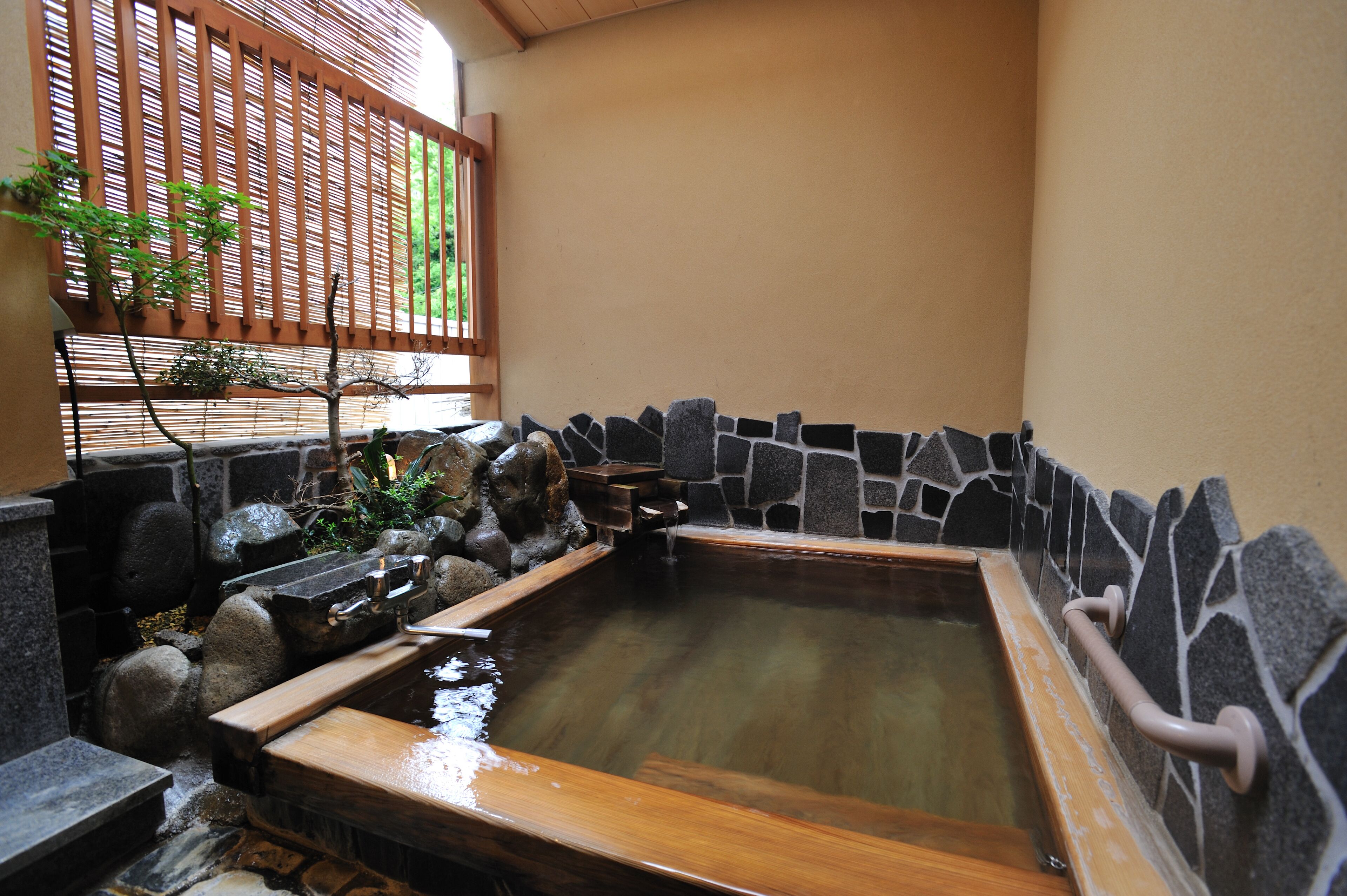 A traditional Japanese onsen with a stone wall, wooden benches, and a wooden bath.