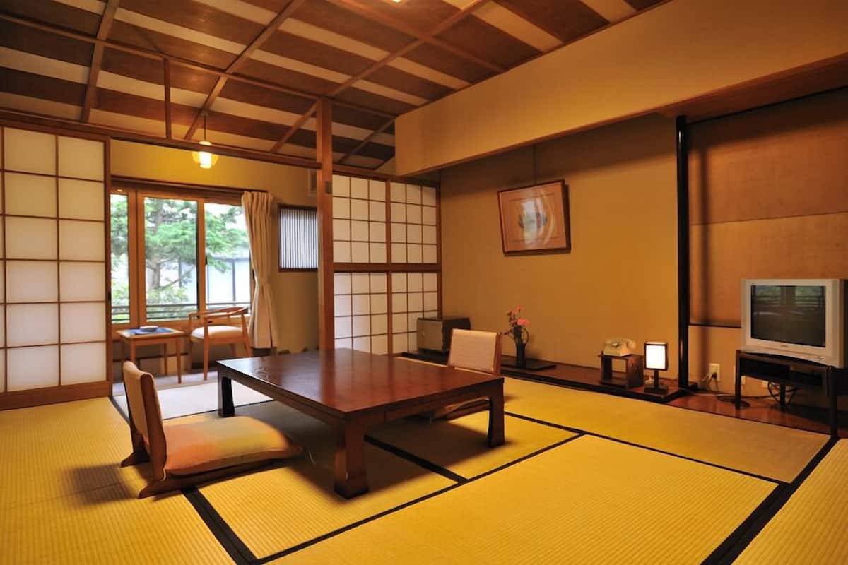 A traditional Japanese room with tatami flooring, a low table, chairs, a television, and a sliding door.