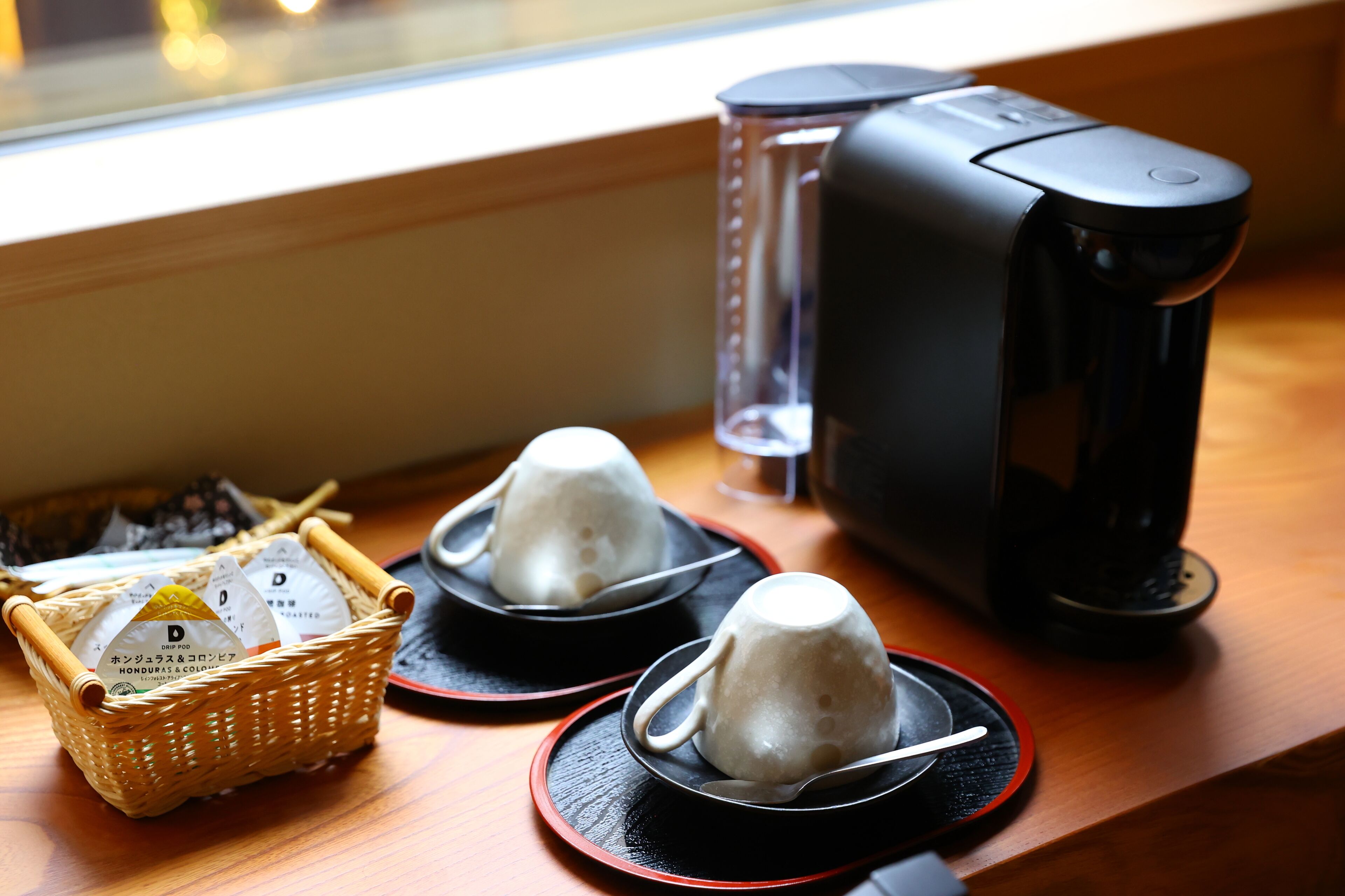 En kaffebryggare, två tekannor och en korg med tepåsar står på ett träbord.