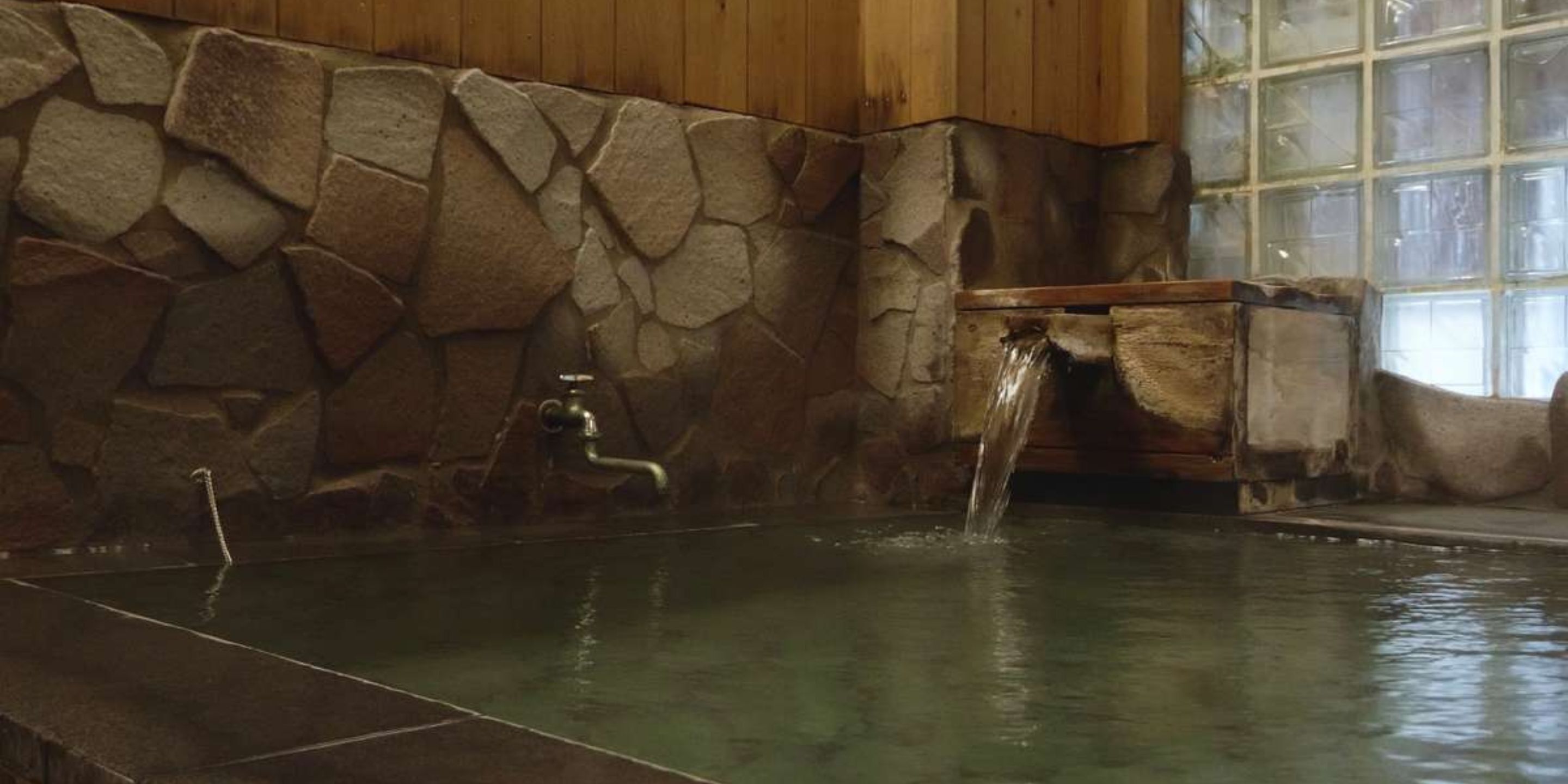 A stone wall with a wooden bench and a water feature.