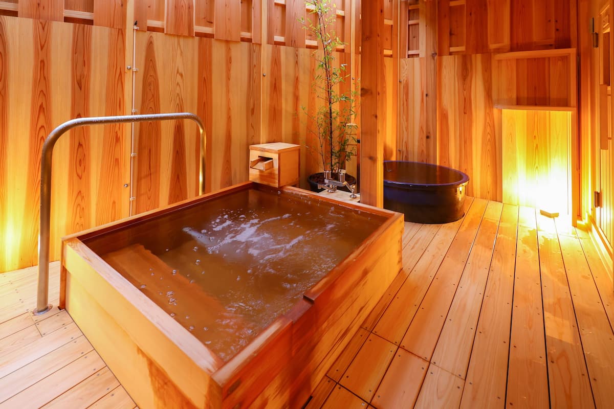 A wooden sauna with a hot tub, a small wooden cabinet, and a potted plant.