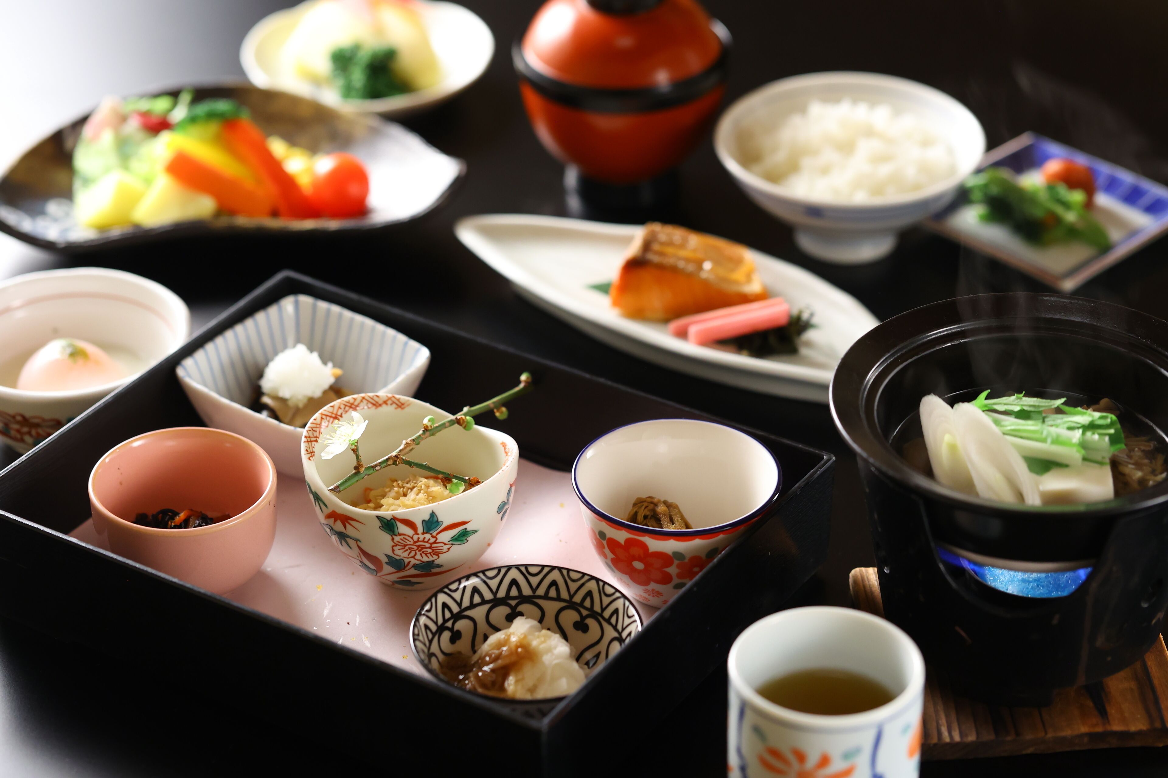 A variety of traditional Japanese dishes arranged on a tray, including rice, vegetables, and a hot pot.