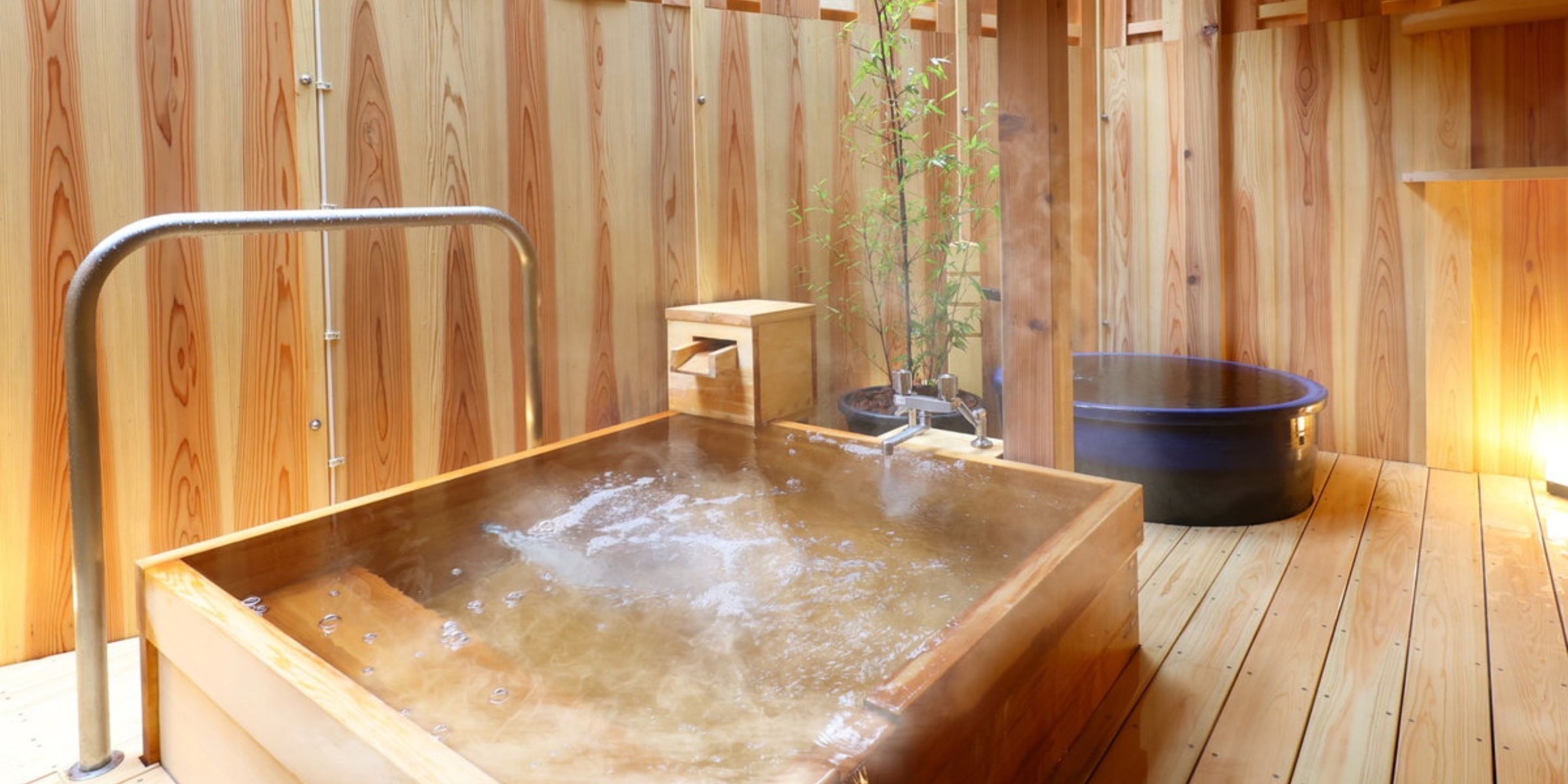 A wooden sauna with a hot tub, a small wooden bench, and a potted plant.
