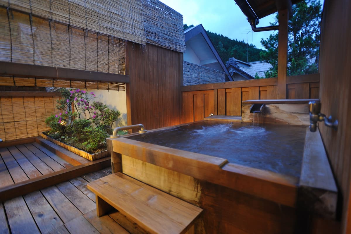 A wooden hot tub with a bench, surrounded by a wooden deck and bamboo walls.