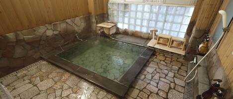 A stone-floored hot tub with a wooden bench and a small table, a stone wall, and a window with a view.