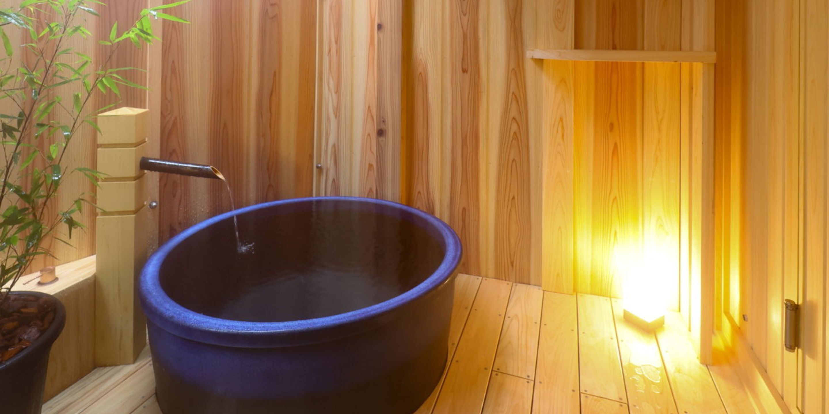 A wooden room with a large black bathtub and a small potted plant.