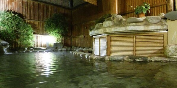 A traditional Japanese onsen with a stone bath, bamboo plants, and a wooden interior.