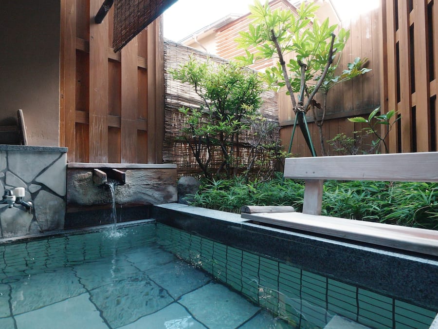 A small outdoor pool with a stone wall and a wooden bench.