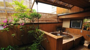 A wooden hot tub in a covered outdoor area with a wooden deck, surrounded by plants and a bamboo fence. - Shibu Onsen KOKUYA (Yamanouchi)