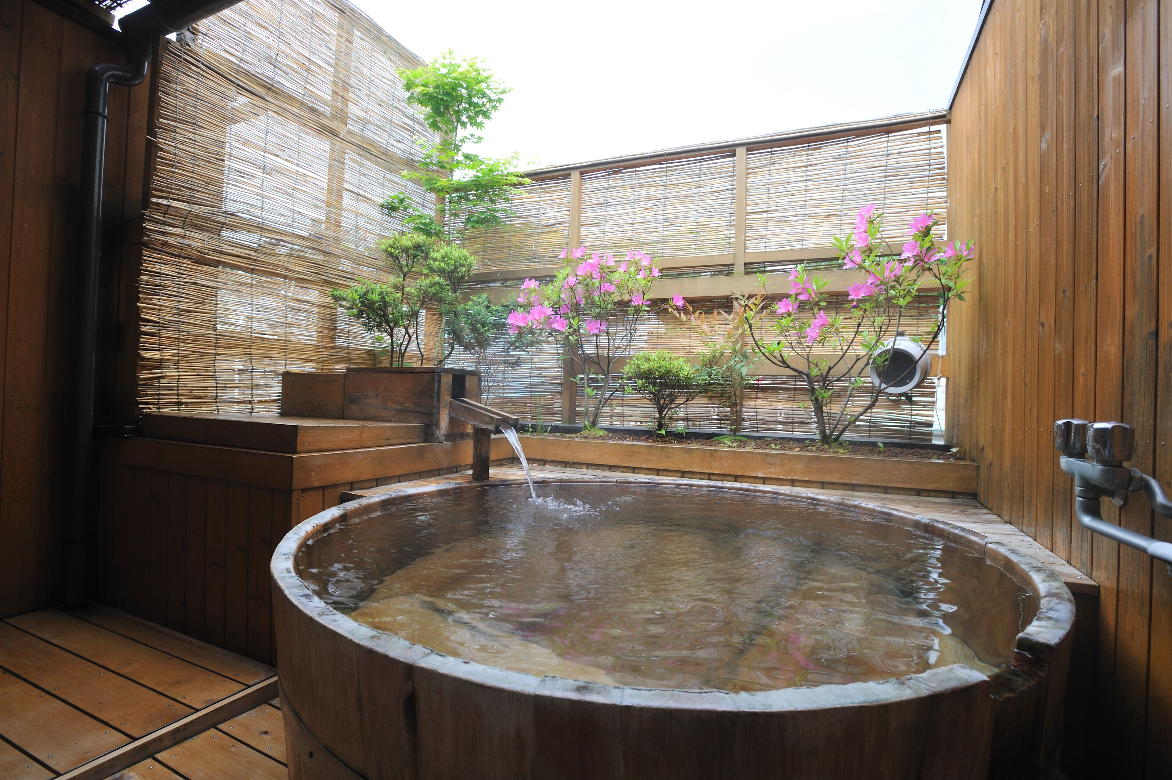 Un bain à remous en bois, doté d’une terrasse en bois, entouré de murs en bambou et d’une clôture en bois.