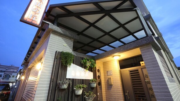 Un bâtiment moderne doté d’une entrée couverte, de plantes en pot et d’une enseigne indiquant la présence d’un restaurant ou d’un café.