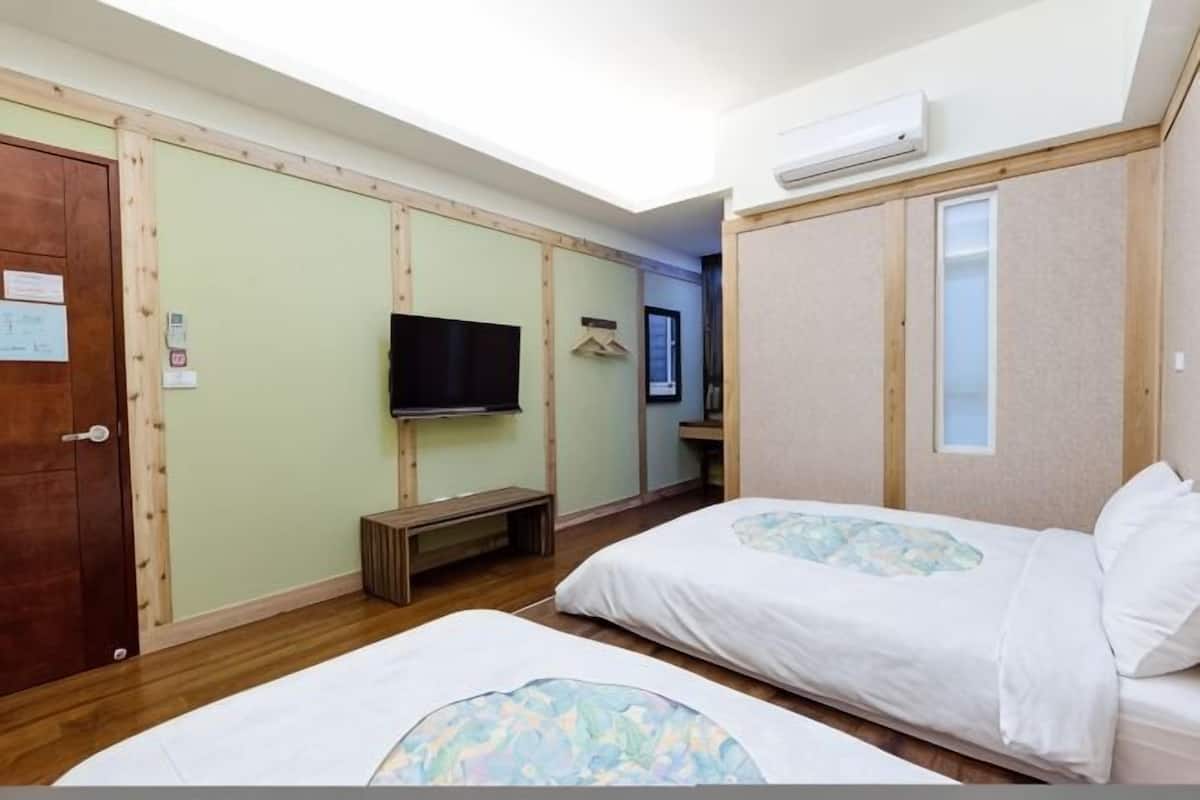 Een hotelkamer met twee bedden, een televisie, een houten deur en een klein bankje.