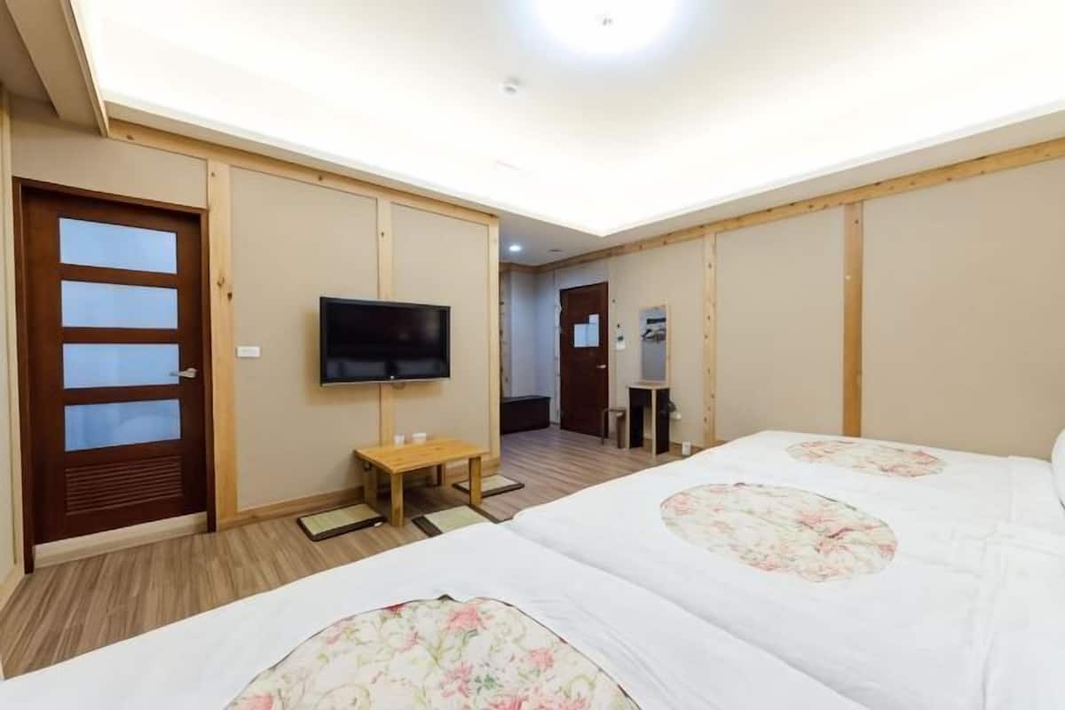 Een hotelkamer met twee bedden, een televisie, een houten deur en een klein tafeltje.