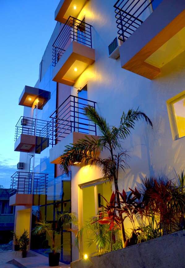 A multi-story building with balconies, a well-lit entrance, and potted plants. - The Orient Beach Boracay (Boracay Island)