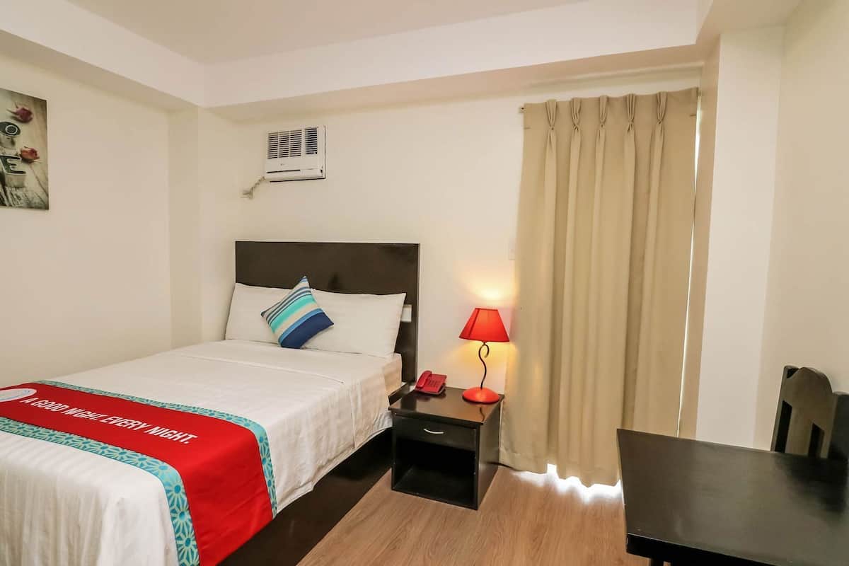 Een hotelkamer met een bed, nachtkastje, lamp en een stoel.