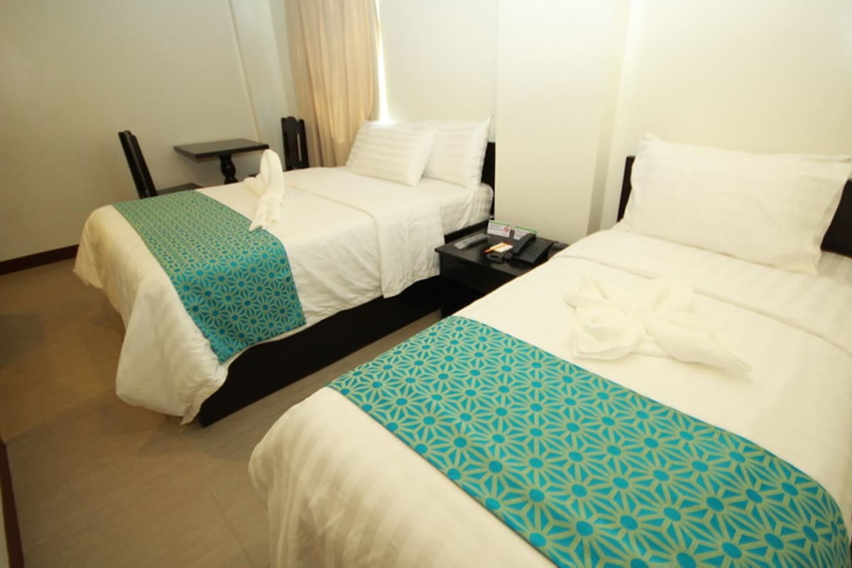 A hotel room with two beds, a small table, and a chair.