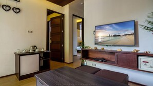 A modern living room with a wooden table, a TV mounted on the wall, and a small refrigerator. - The Orient Beach Boracay (Boracay Island)