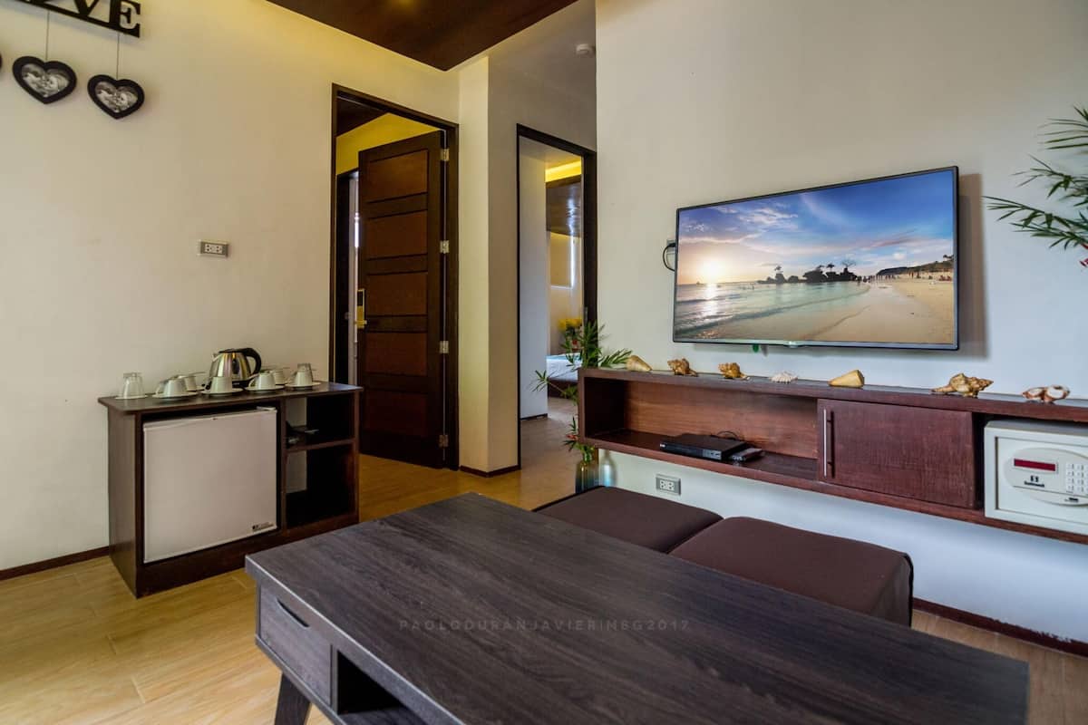 Een moderne woonkamer met een houten tafel, een aan de muur bevestigde televisie en een kleine koelkast.