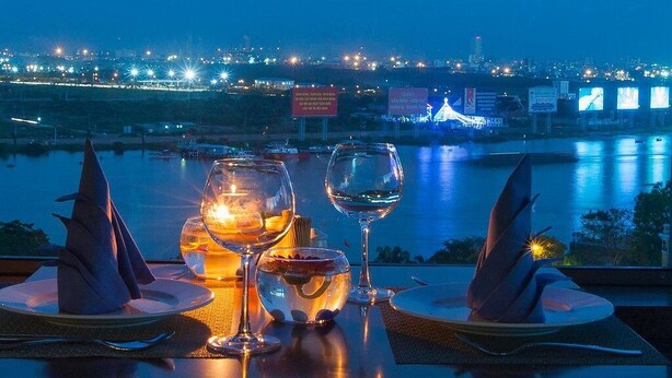 Mesa para dos con copas de vino y una vela, con vista a un paisaje urbano nocturno.