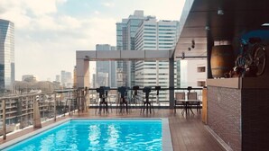 Una piscina en la azotea con asientos tipo bar y vista al horizonte de la ciudad.