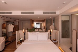Una habitación de hotel moderna con una cama grande, un vestidor, un baño con ducha y vistas a la ciudad.