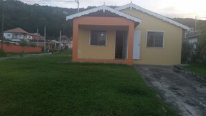 A small, single-story house with a porch, a door, and two windows. - Palm Cove - 2 Bedroom Cottage (Montego Bay)