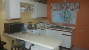 A compact kitchen with white cabinets, a gas stove, a toaster, and a sink. - Palm Cove - 2 Bedroom Cottage (Montego Bay)