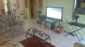 A living room with a sofa, a coffee table, a television, and a fan. - Palm Cove - 2 Bedroom Cottage (Montego Bay)