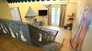 Una escalera conduce a una habitación con televisor, una ventana con cortinas y un cuadro en la pared.