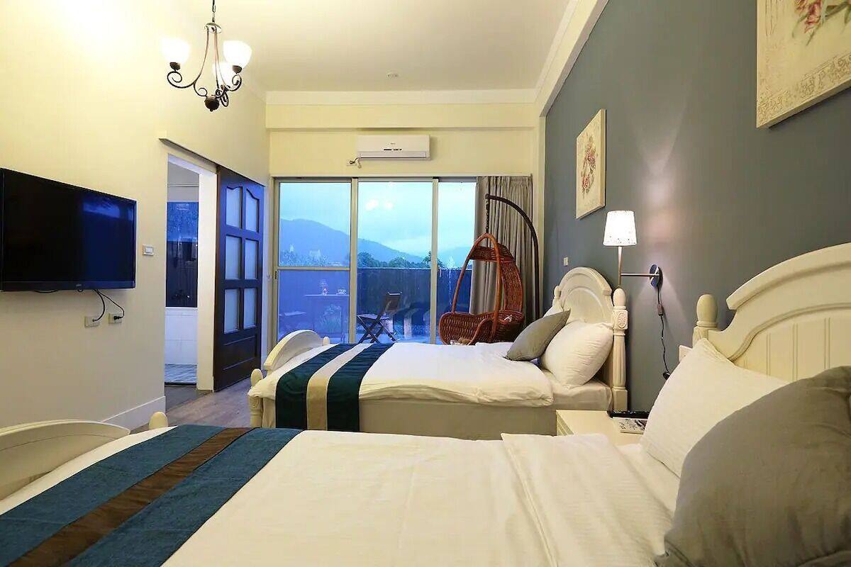 A hotel room with two beds, a TV, a chandelier, and a balcony with a view.