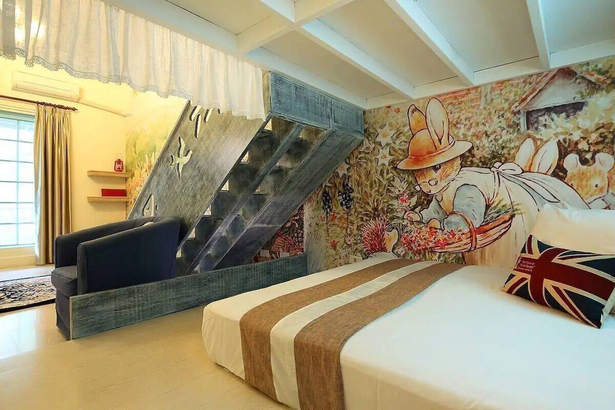A bedroom with a bed, a sofa, a unique staircase, and a mural.