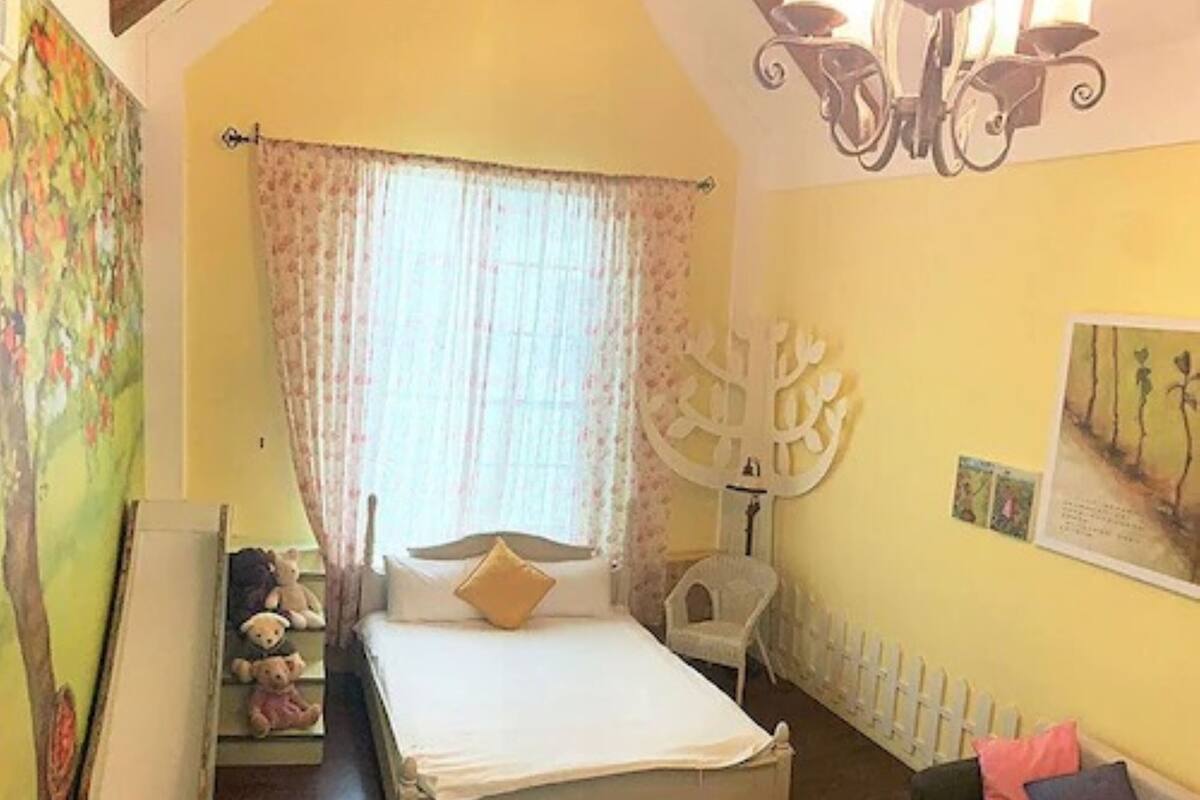 A bedroom with a bed, a bench, a sofa, a chair, and a wall with a tree decoration.