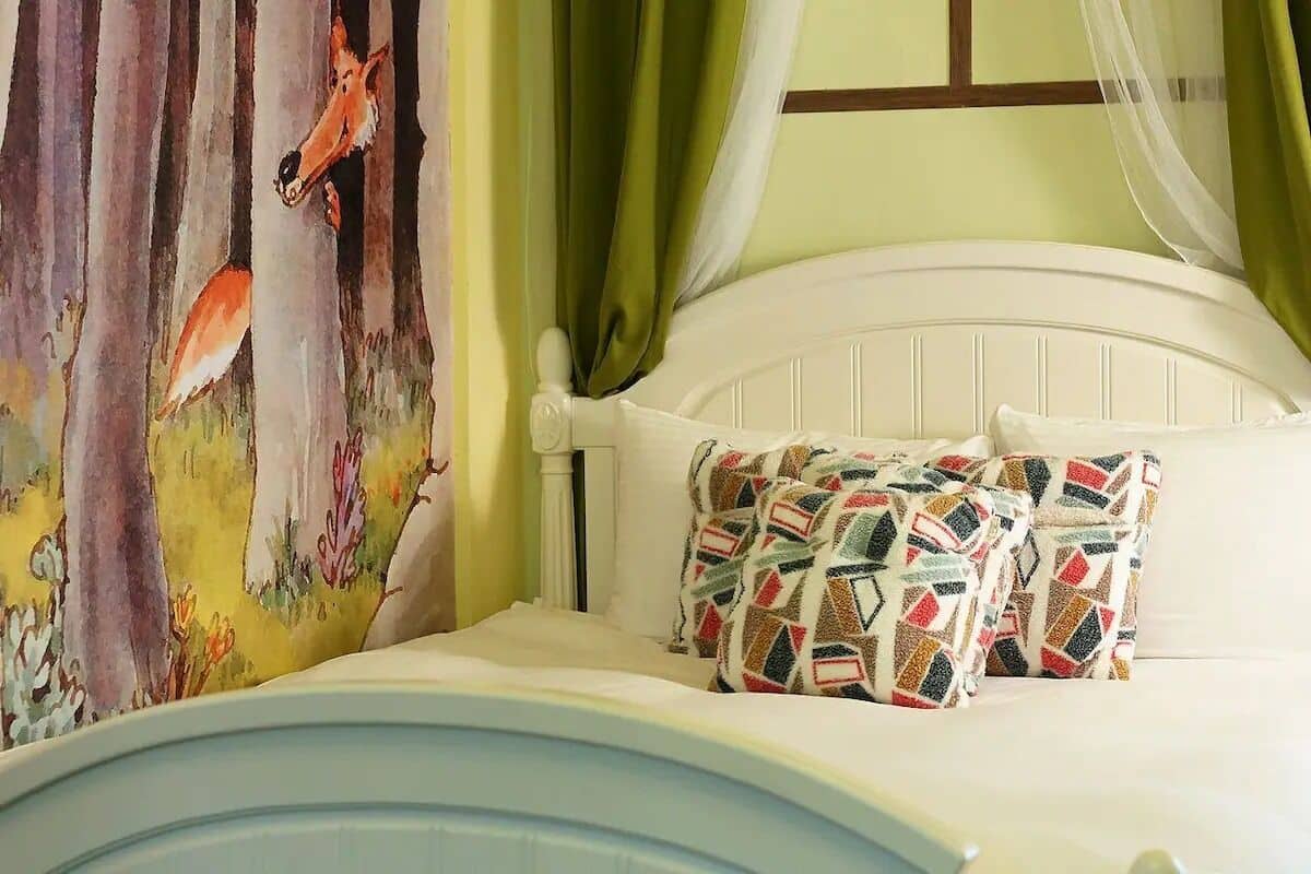 A bed with a white headboard, a colorful pillow, and a painting of foxes on the wall.