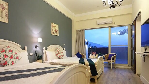 Habitación de hotel con dos camas, una silla, un televisor y un balcón con vistas.