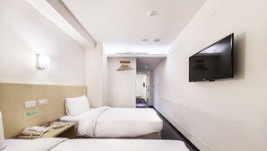 A hotel room with two beds, a flat-screen TV mounted on the wall, a bedside table with a phone and a cup, and a small desk with a chair.