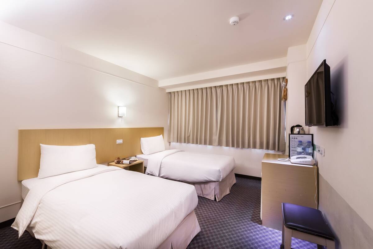 Habitación de hotel con dos camas, un escritorio con computadora y un televisor montado en la pared.