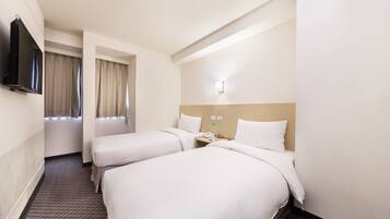 A hotel room with two beds, a TV, a bedside table with a phone, and a window with curtains.